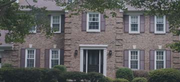 Picture of a large, two story story brickhouse with burgundy shutters surrounded by bushes.